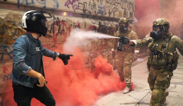 A federal officer pepper sprays a protester in front of the Federal Courthouse in Portland (Photo by Nathan Howard/Getty Images)
