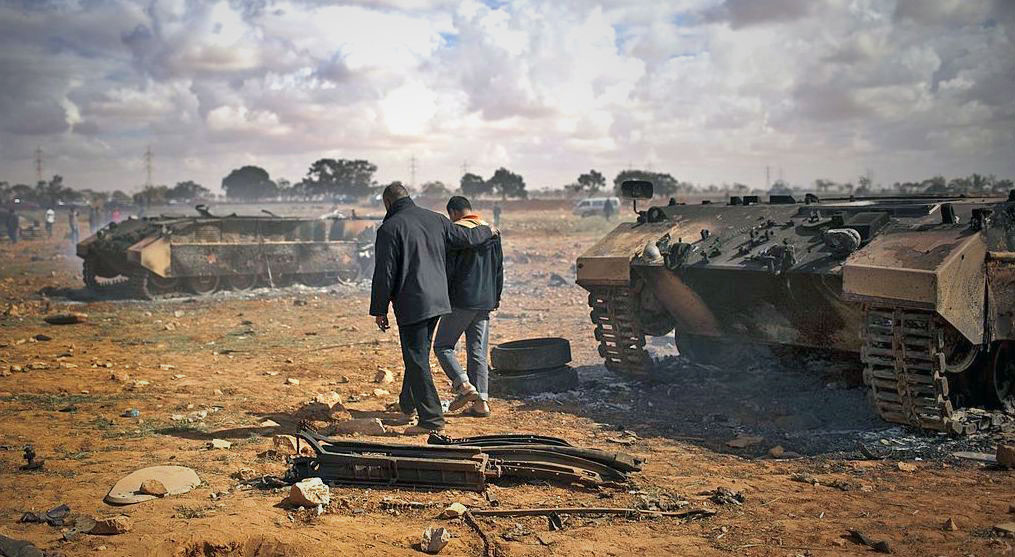 Libyan civilians walk and climb on the rubble of destroyed pro-Gaddafi army vehicles. Credit: Getty