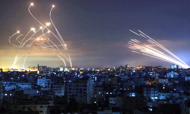 The Israeli Iron Dome (left) intercepts rockets fired by Hamas (right) (Photo by ANAS BABA/AFP via Getty Images)