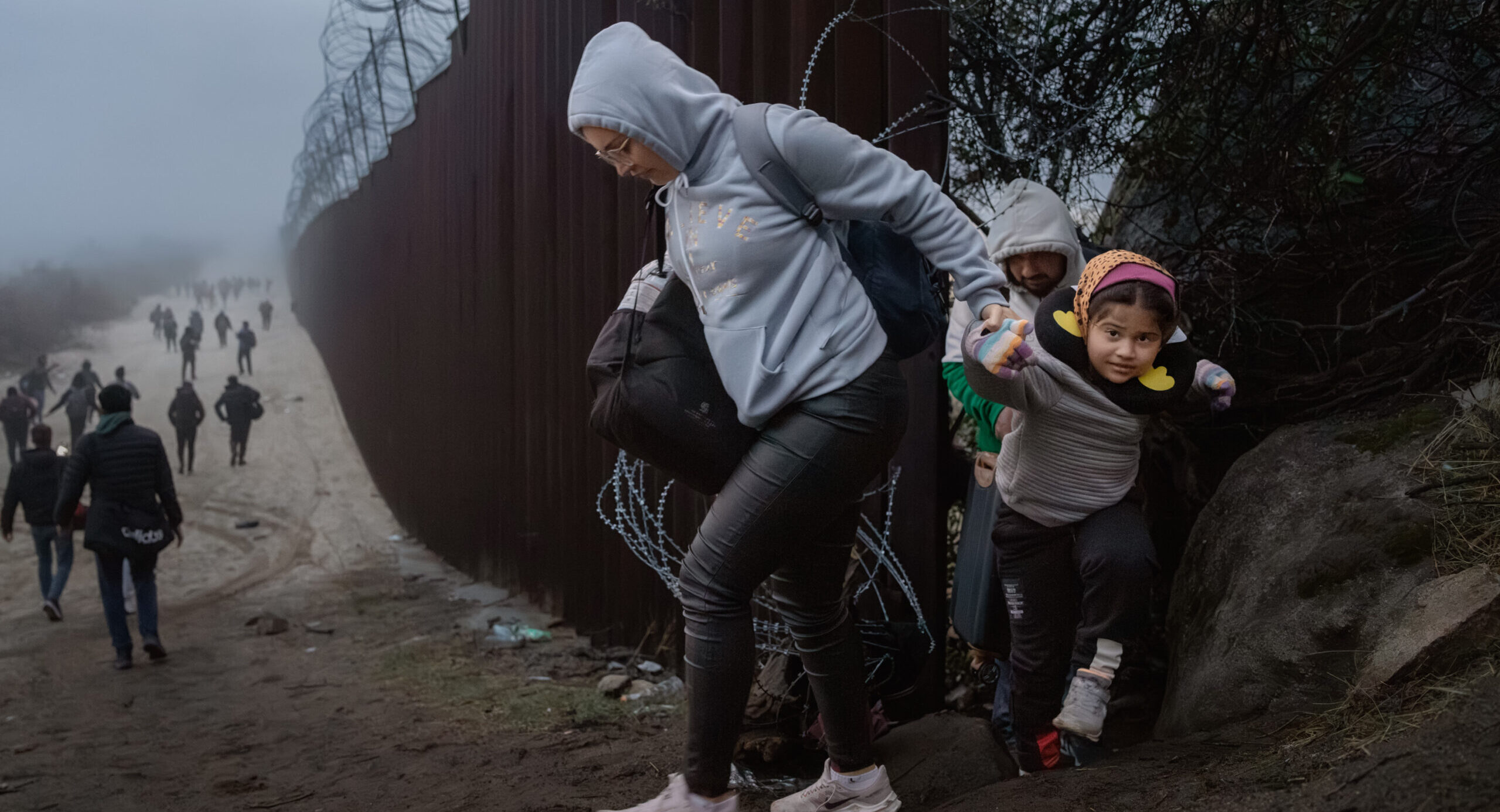 Migrants cross through a gap in the US-Mexico border fence in December. Credit: Getty