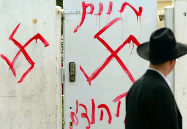 A Jewish man looks at antisemitic graffiti sprayed on the gate of a synagogue in 2006 in Petah Tikva, near Tel Aviv, in central Israel. (Uriel Sinai/Getty Images)